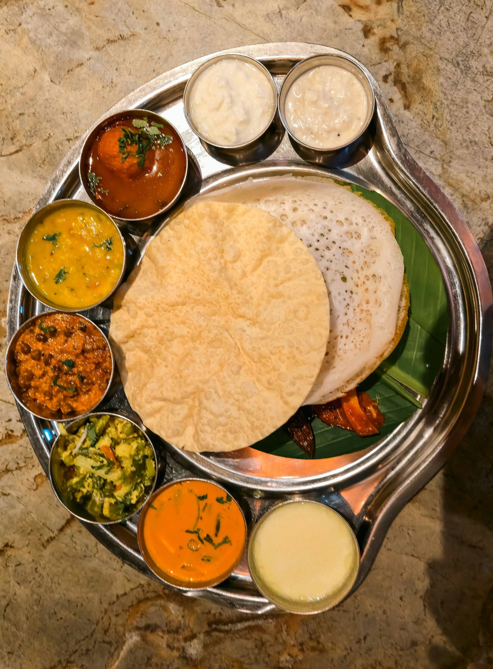 Lace-edged appam with vegetable curries on a steel thali