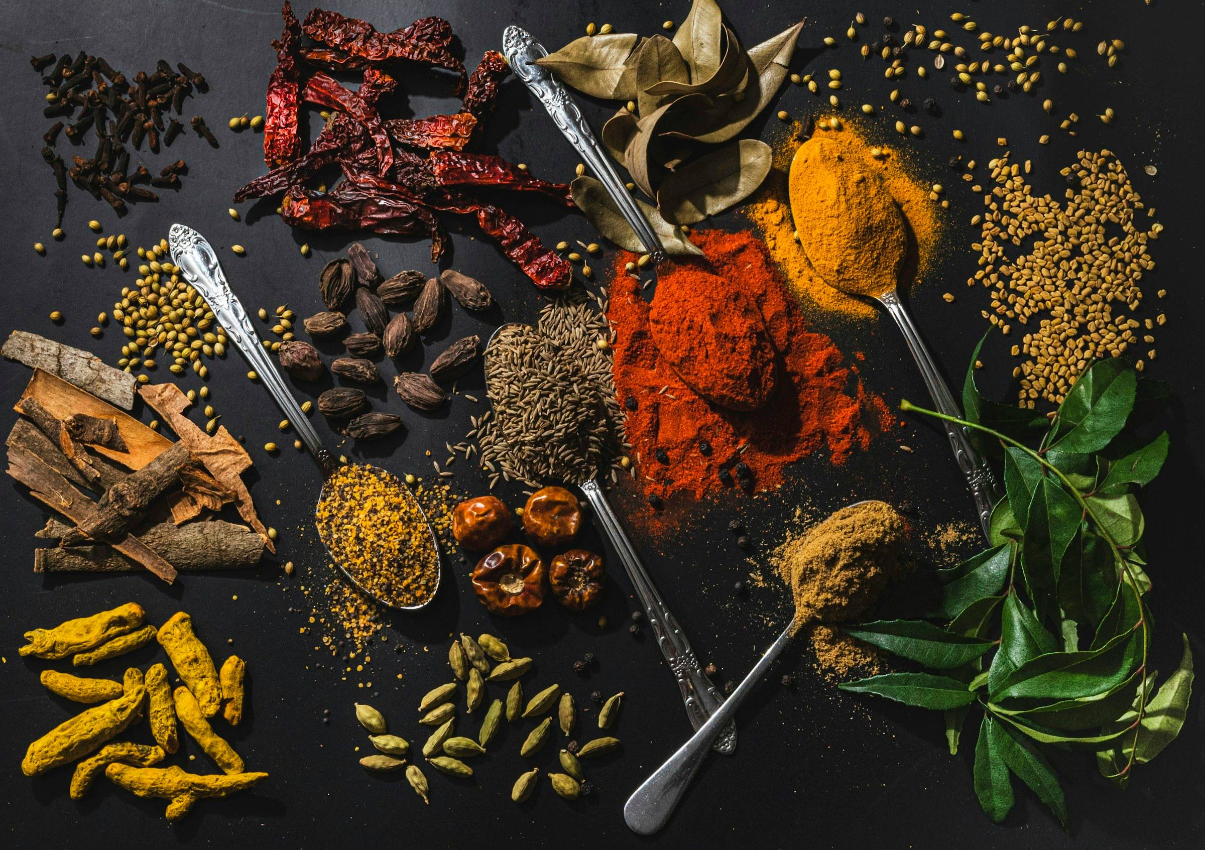 Whole and ground spices, curry leaves and turmeric root arranged on a dark surface